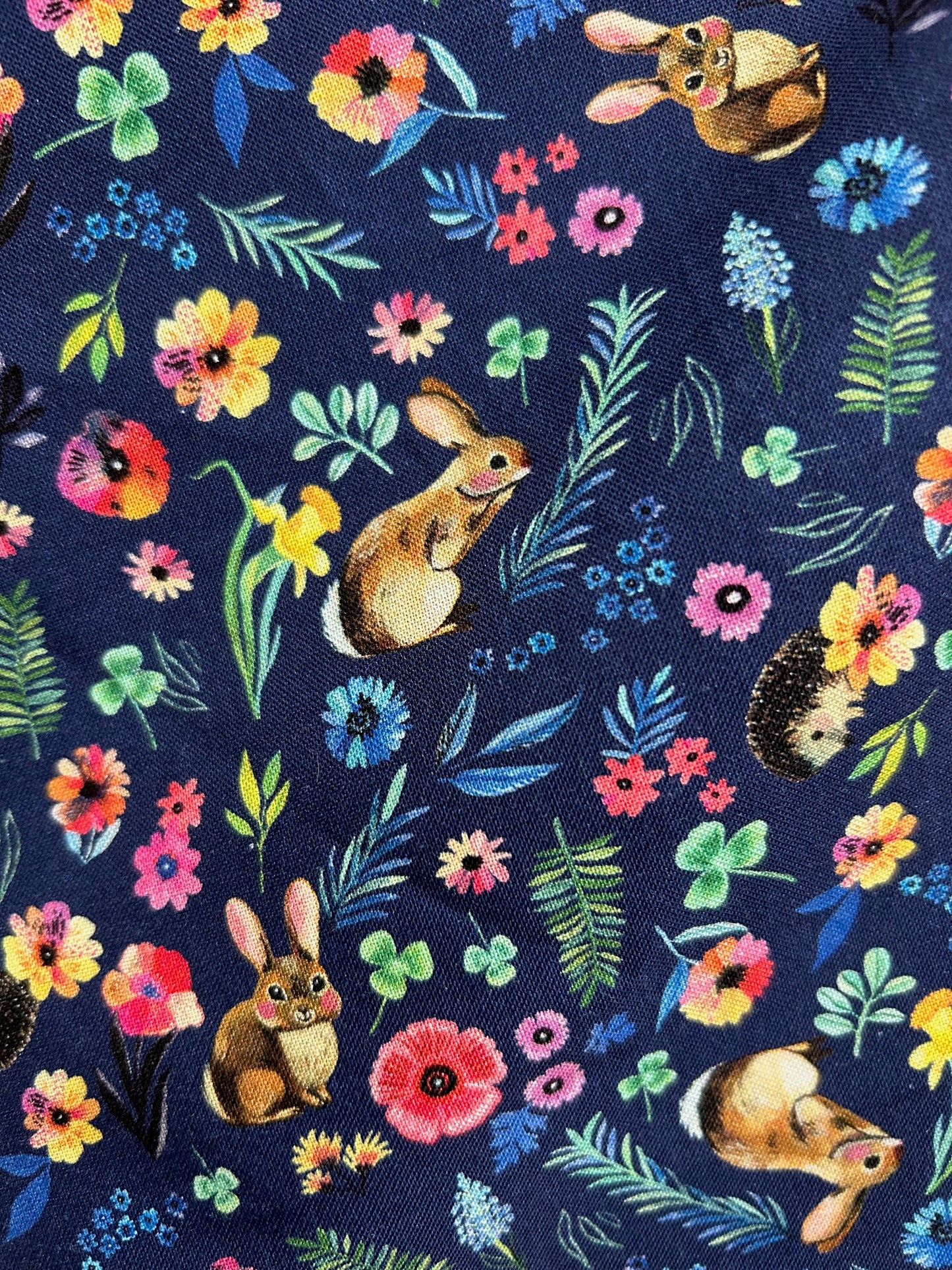 close up of fabric showing bunnies, hedgehogs and flowers on navy background
