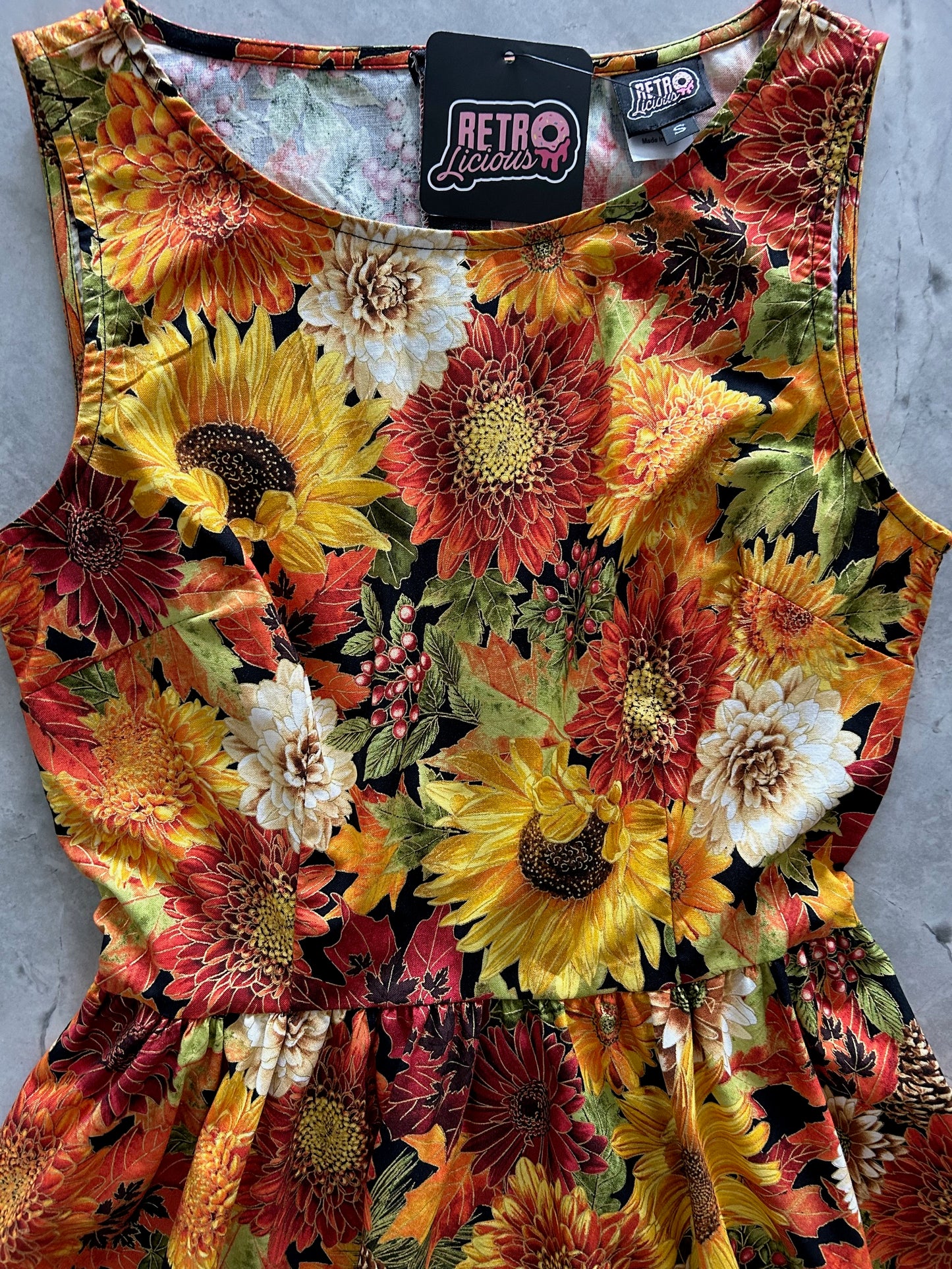 Floral patterned dress with sunflowers and autumn colors on a grey surface.