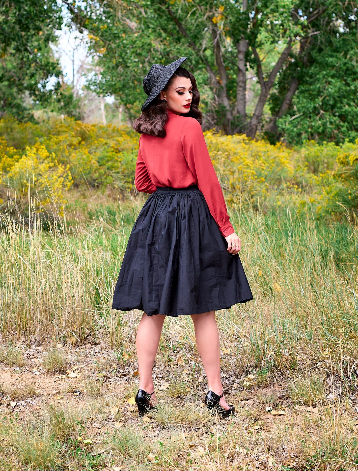 a full size image of the back view of a model standing in front of trees wearing the helen retro blouse in cognac