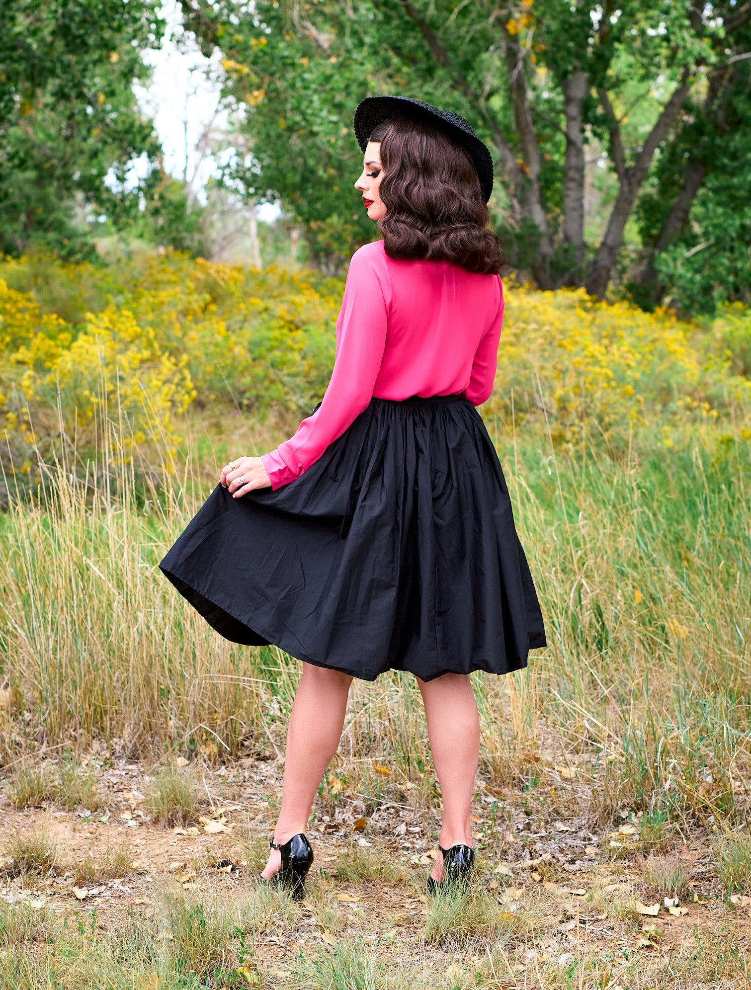 a full length of the back view of a model standing in front of trees wearing the helen retro blouse in pink
