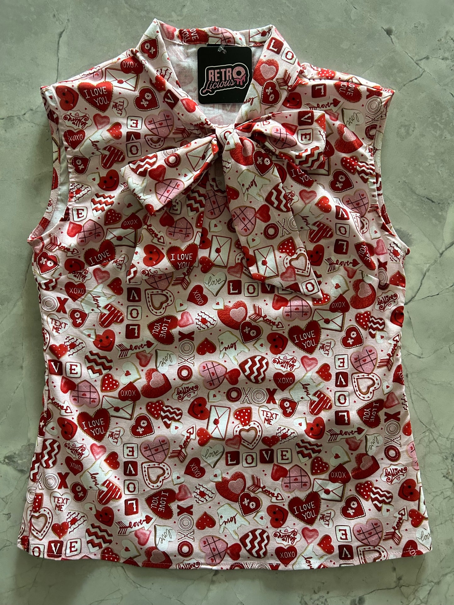 a flat lay of our sleeveless bow tie blouse with xoxo hearts and love fabric