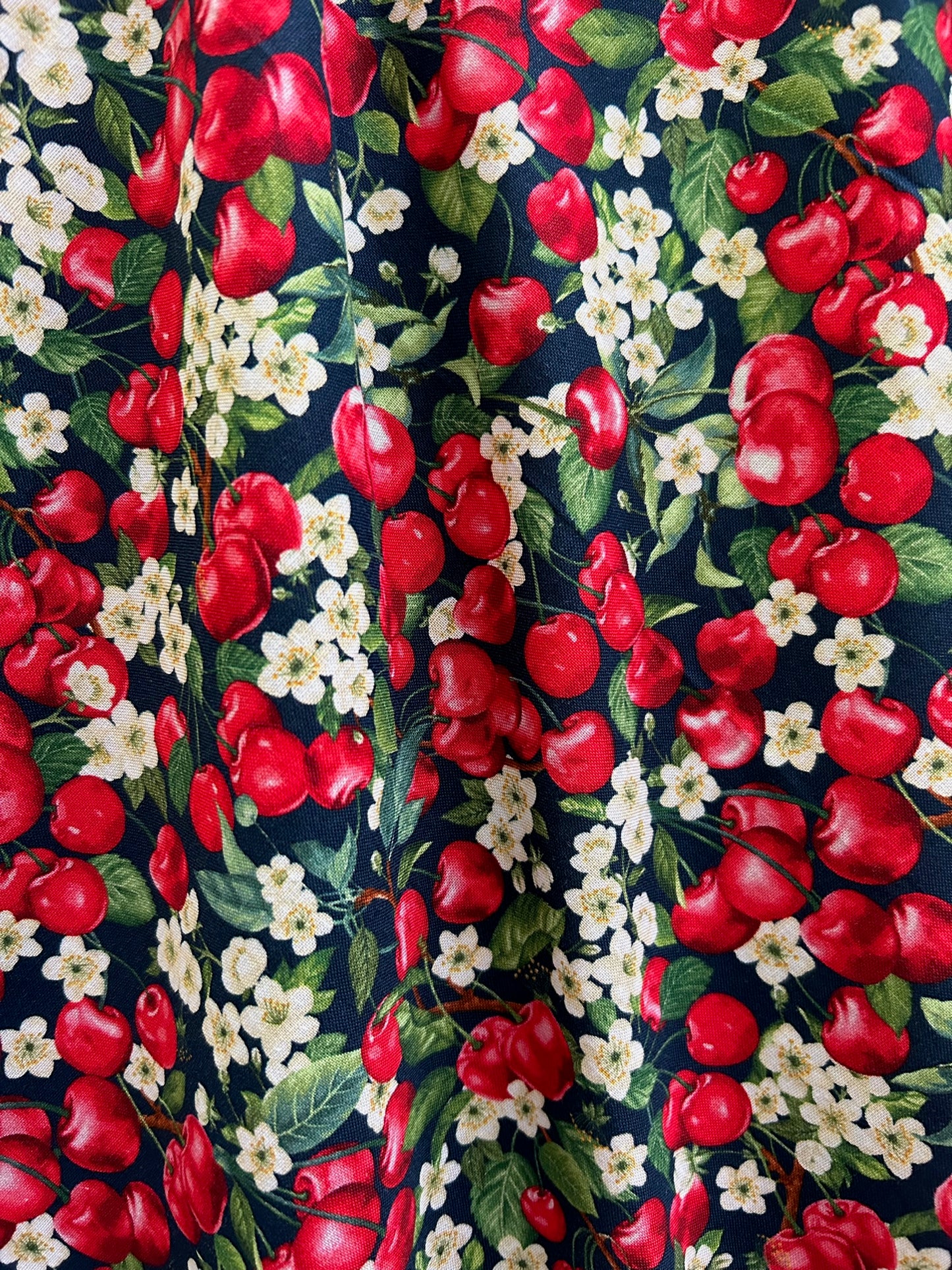 a close up of the fabric of the cherry good vintage dress showing tossed cherries and cherry blossoms