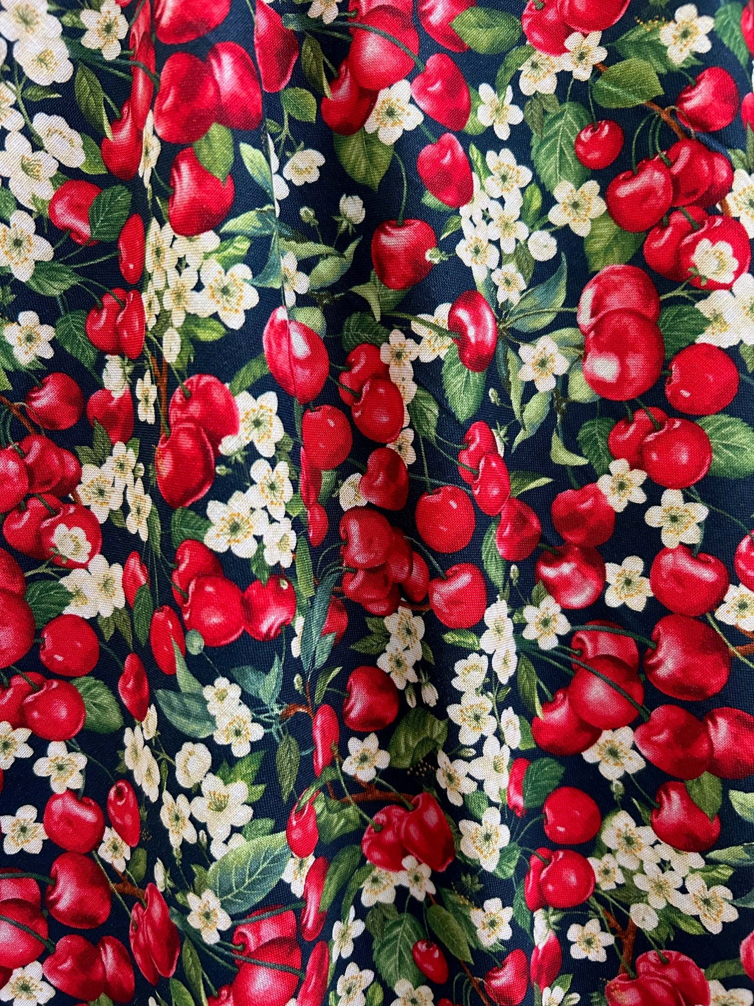 a close up of the fabric of the cherry good vintage dress showing tossed cherries and cherry blossoms 