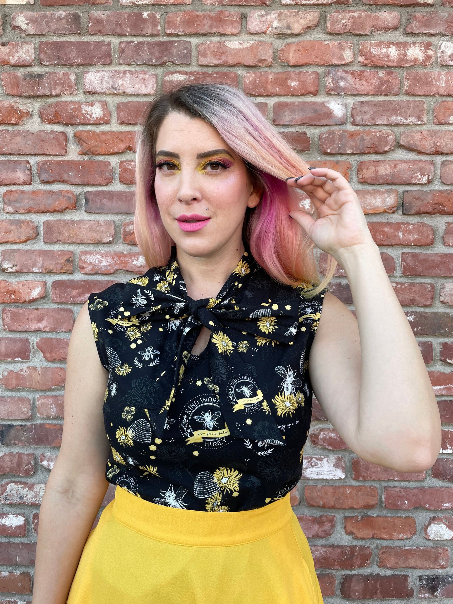 a close up of a model standing in front of a brick wall wearing our bee kind bow top