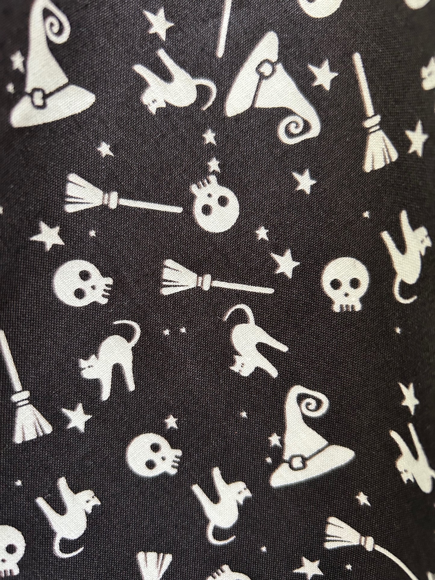 a close up of the fabric swatch showing a white tossed print of skulls, witch hats, broomsticks, stars and cats on black background 