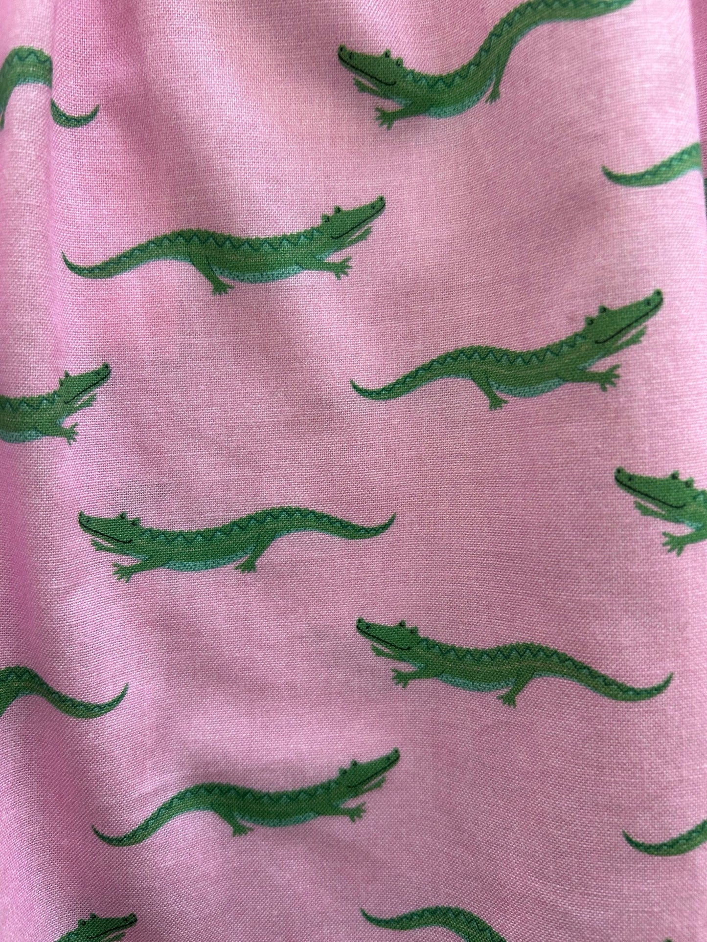 close up of fabric with green alligators on pink background