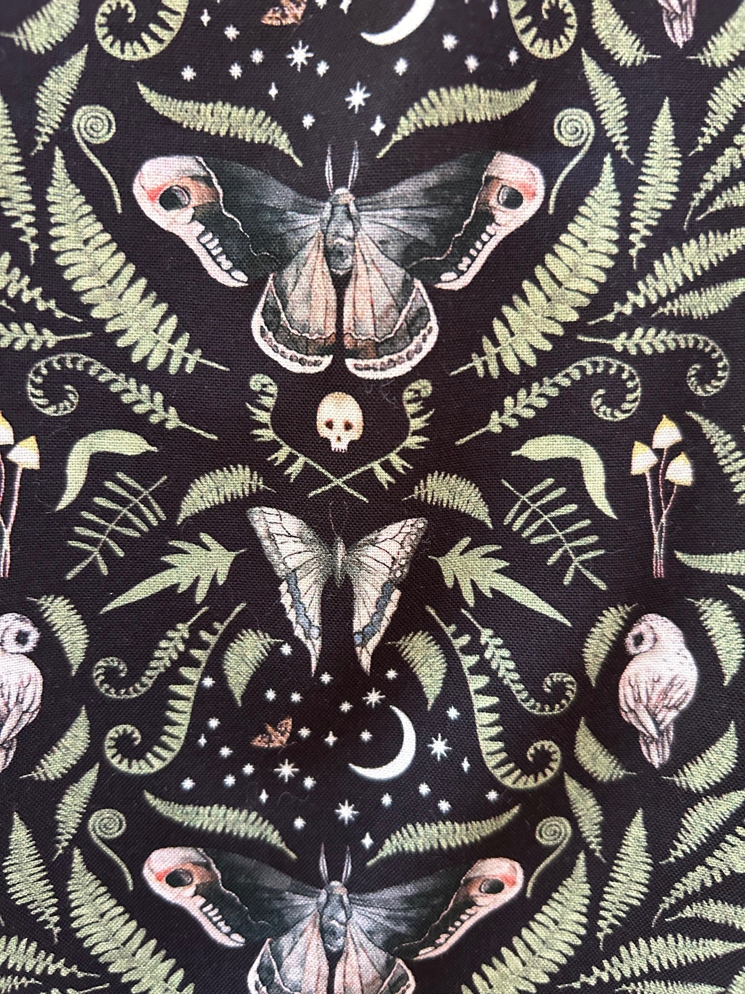 a close up of the print on the fabric showing moths, skulls, owls and leaves on black background