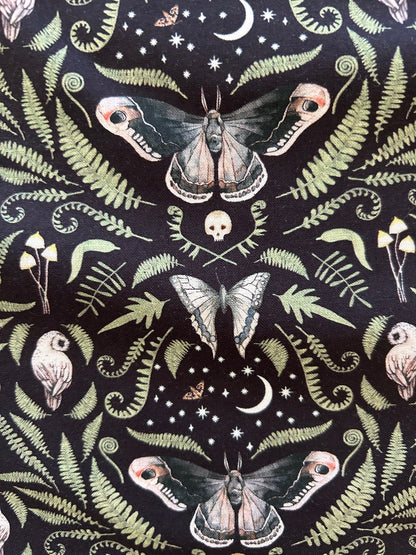 a close up of the fabric on black bacground showing details of moths, skulls, leaves and owls
