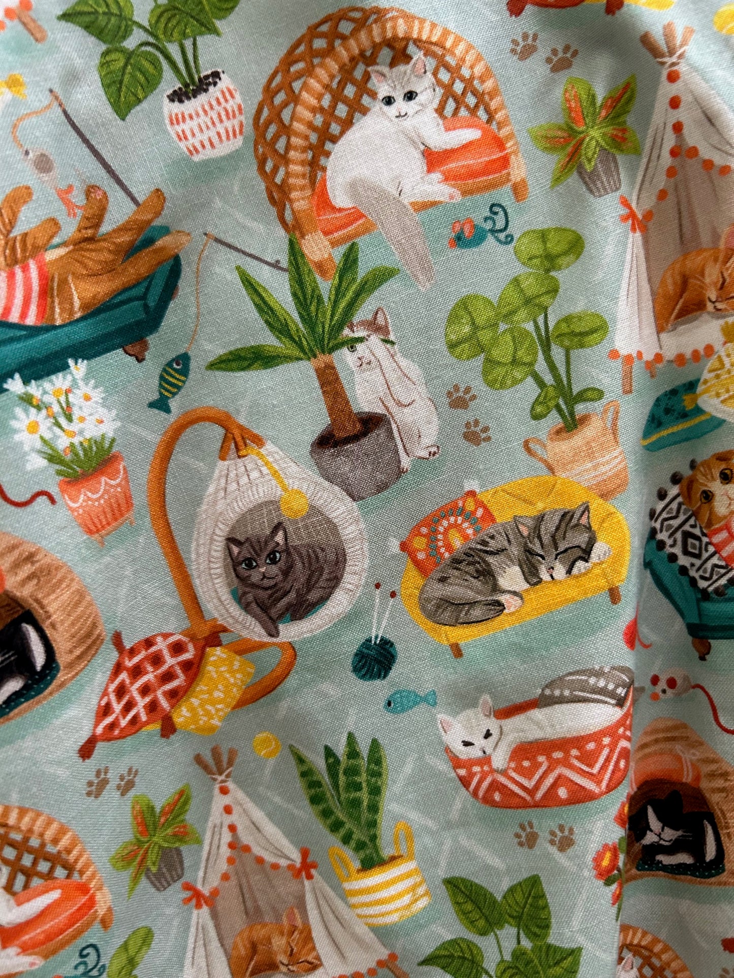 a close up of fabric showing cats lounging and house plants on light green background