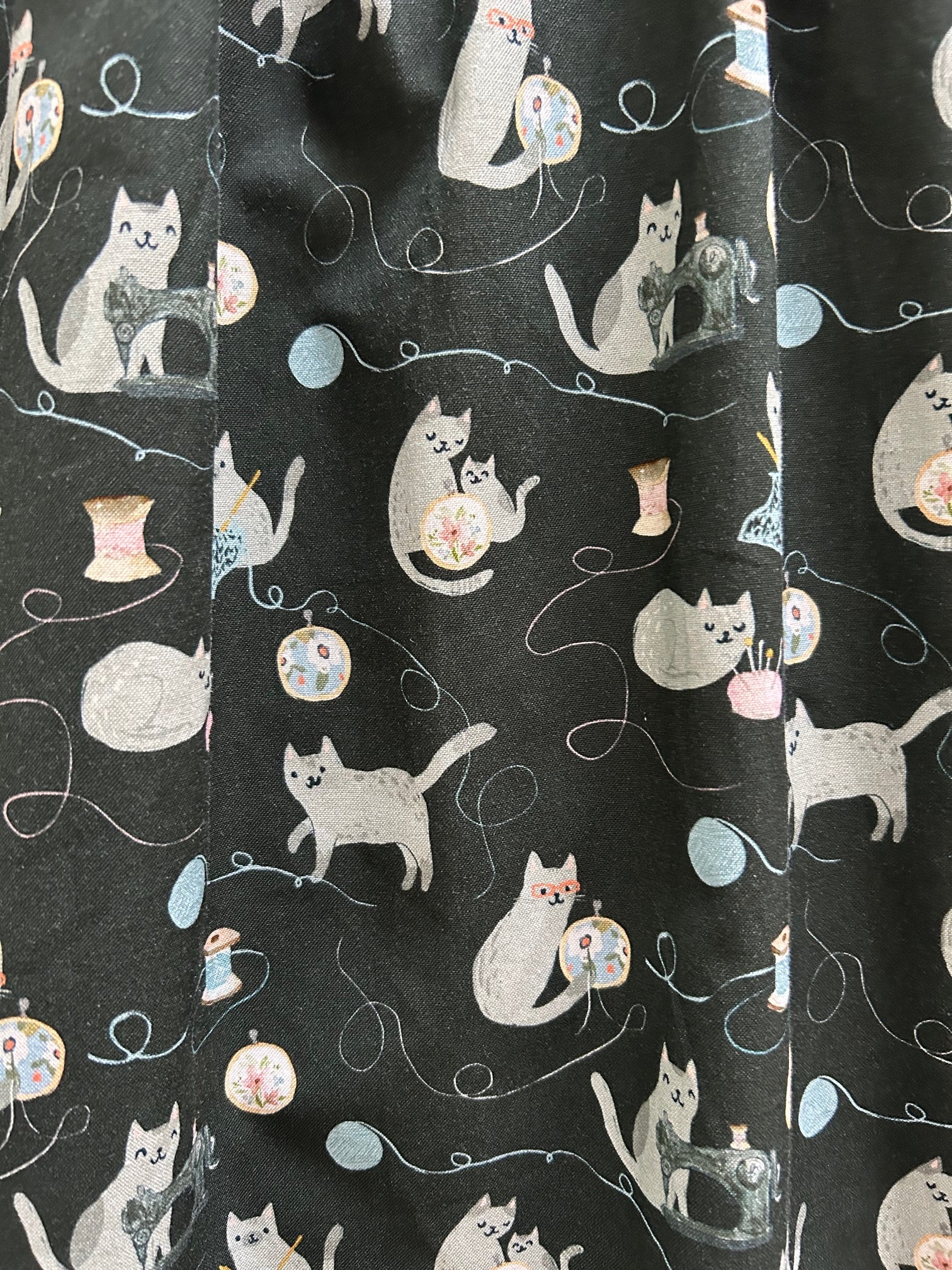 close up of fabric showing cats and thread and yarn on dark navy background