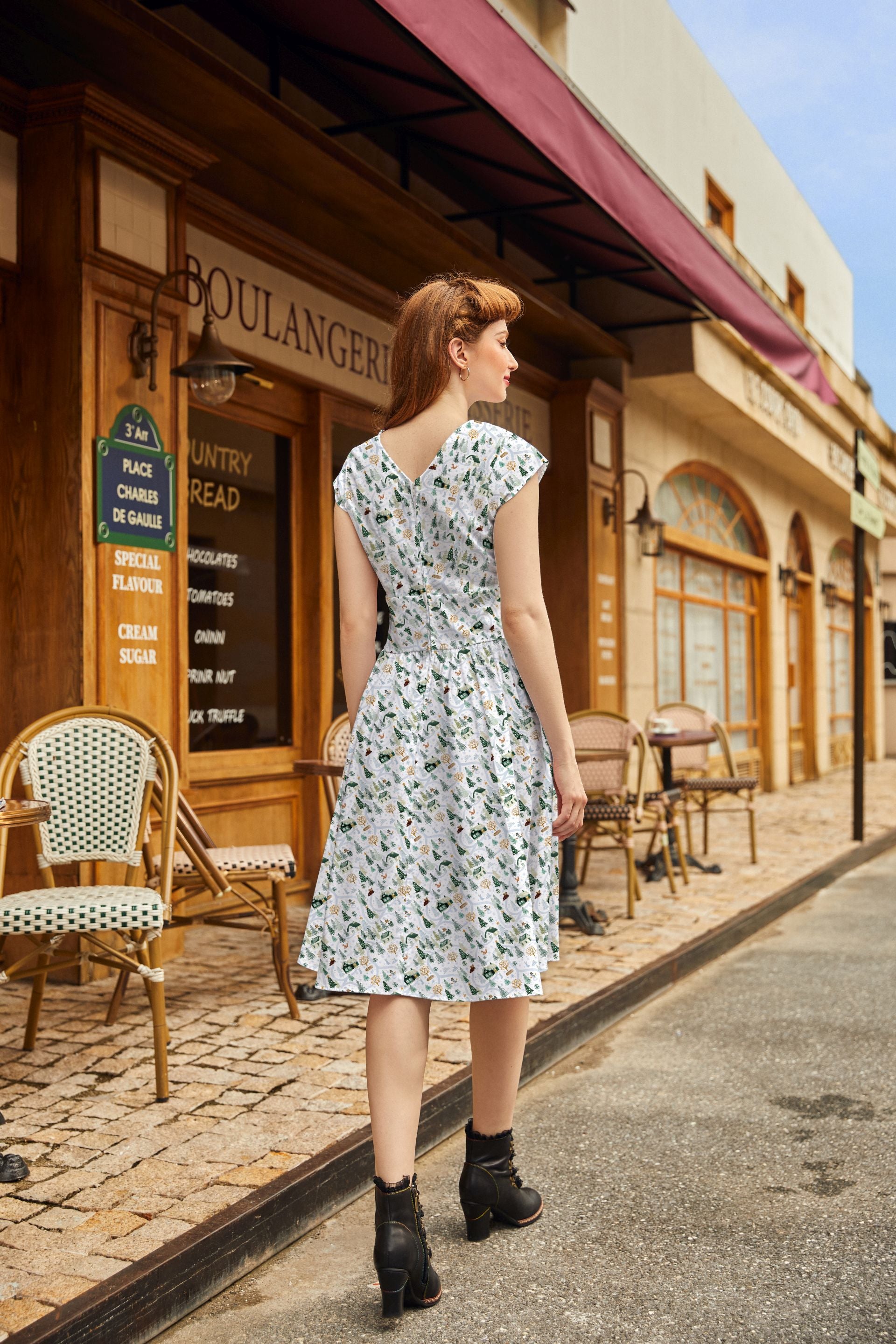 Woman in a floral dress standing on a street in front of a bakery.