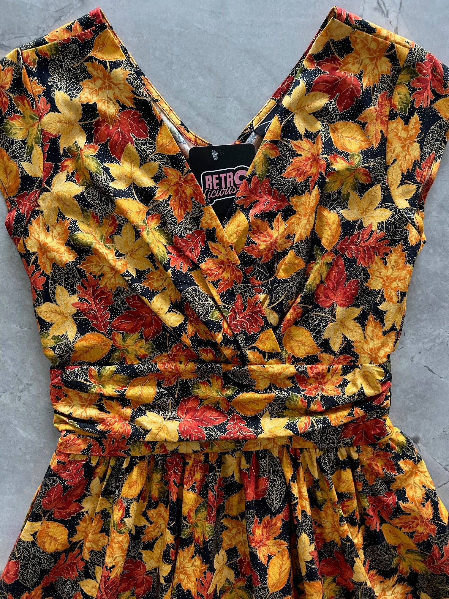 close up of autumn leaf pattern greta dress on a gray surface