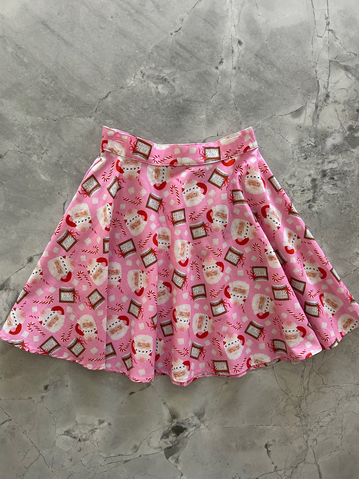 flatlay of pink background with tossed santa heads and hot cocoa skater skirt