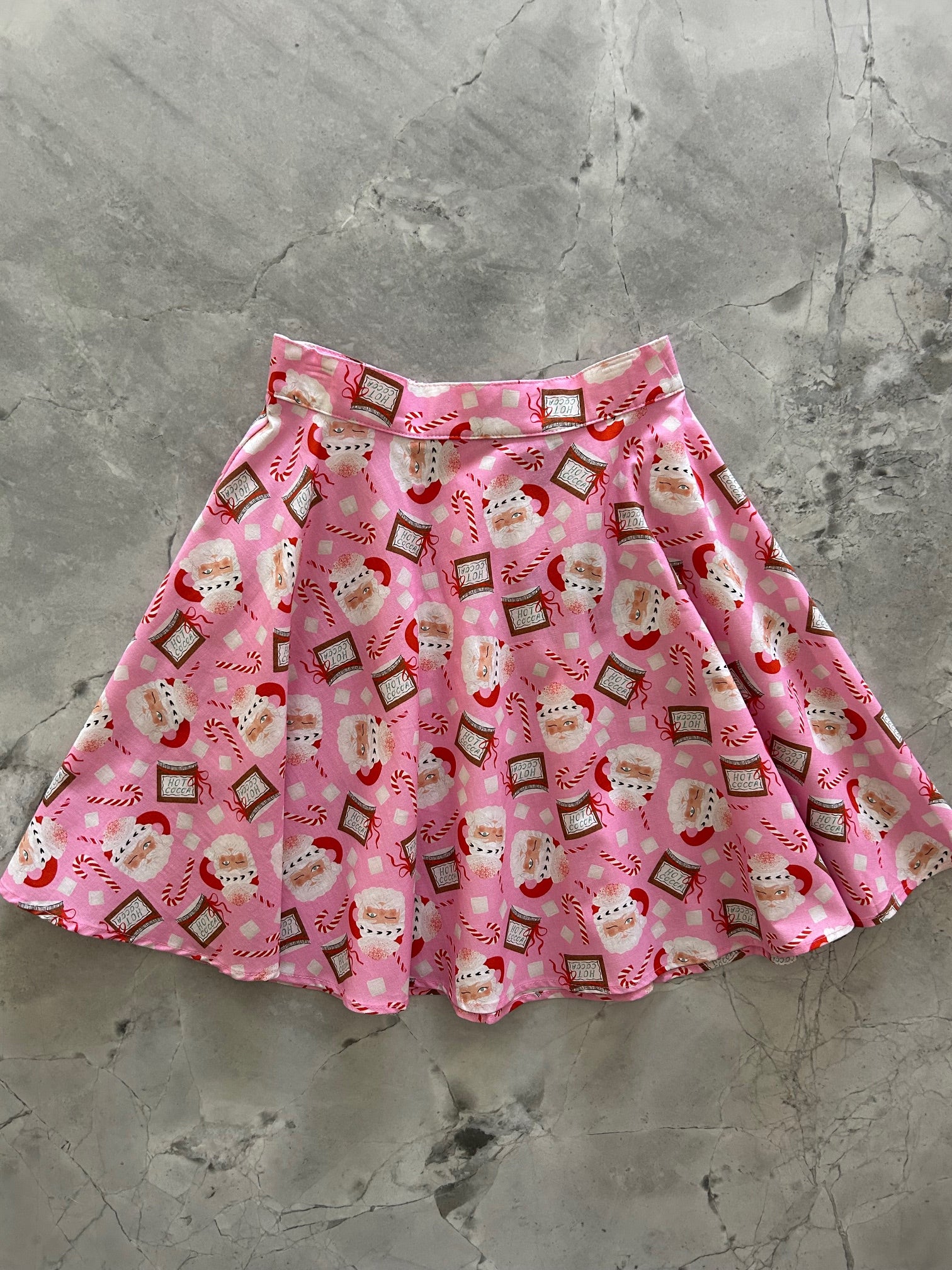 flatlay of pink background with tossed santa heads and hot cocoa skater skirt