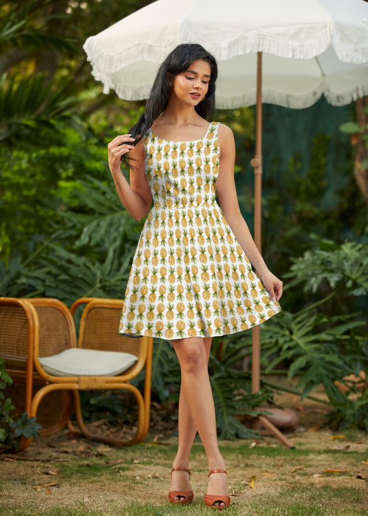 Woman in a pineapple-patterned dress standing under a white umbrella in a garden setting.