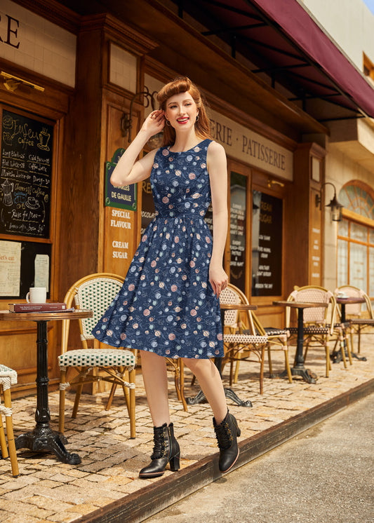 Woman in a blue floral dress standing in front of a patisserie.