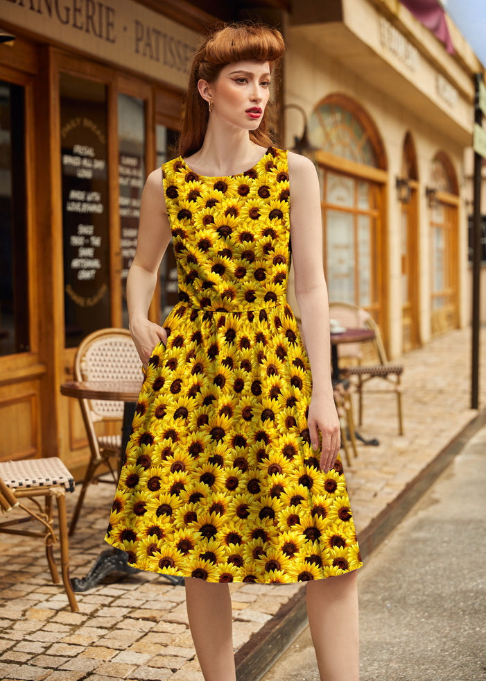 Woman wearing a yellow dress with black flower pattern on a street.