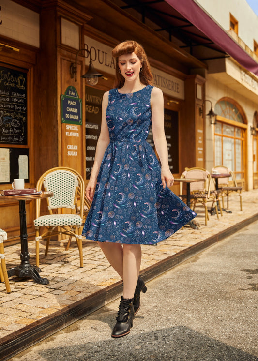 Woman in a blue celestial print dress standing on a street with a café in the background
