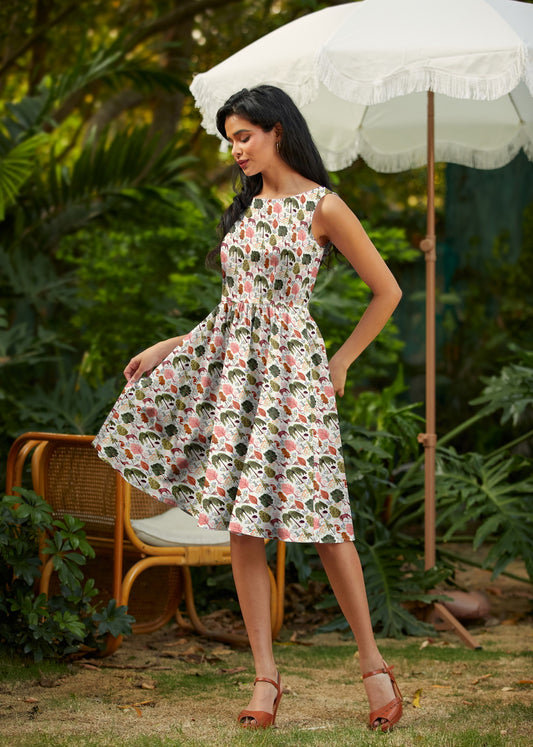 Woman in a floral dress standing outdoors with a white umbrella and chair in the background.