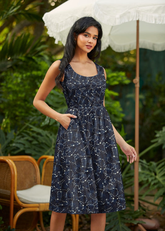 Woman wearing a navy blue dress with white patterns outdoors under a white umbrella.