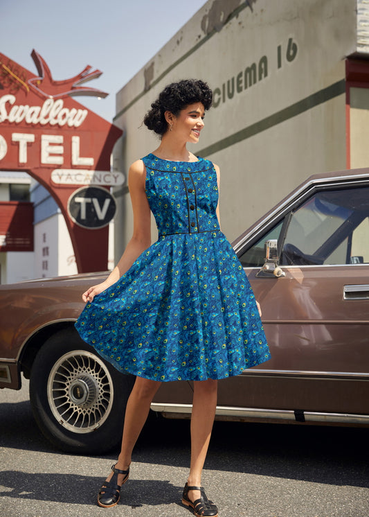 Woman in a blue dress standing next to an old car with a motel sign in the background