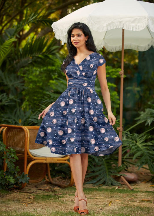 Woman in a blue dress with a floral pattern standing outdoors under a white umbrella.