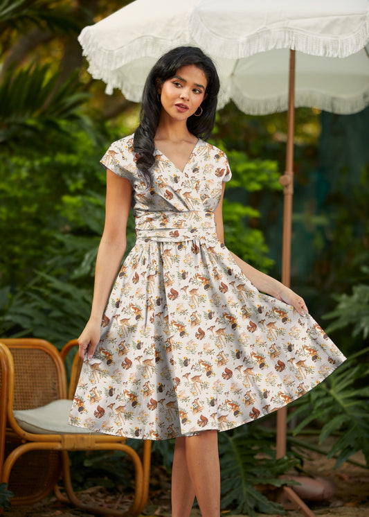 Woman in a floral dress standing outdoors with greenery and an umbrella in the background