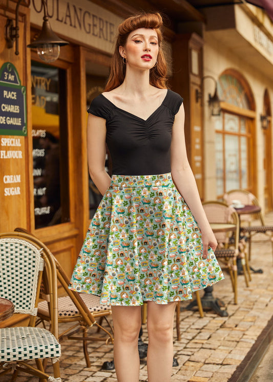 Woman in a black top and patterned skirt standing in front of a bakery.