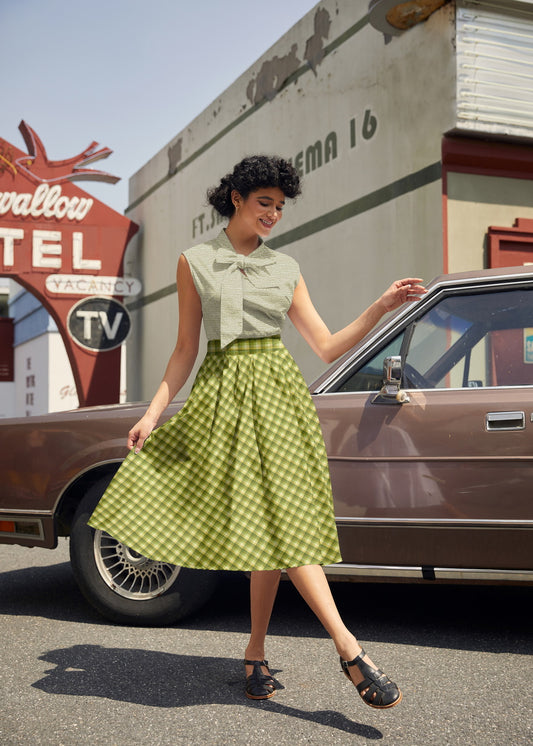 Woman in vintage attire standing next to a classic car with a motel sign in the background