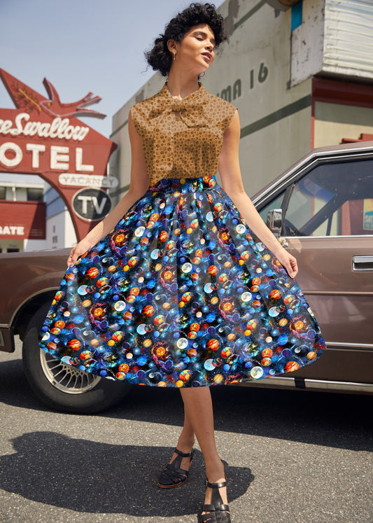 Woman in a patterned dress standing in front of a vintage car with a motel sign in the background