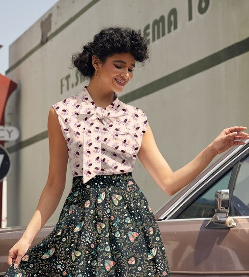 Woman in a floral dress standing next to a vintage car with a building in the background