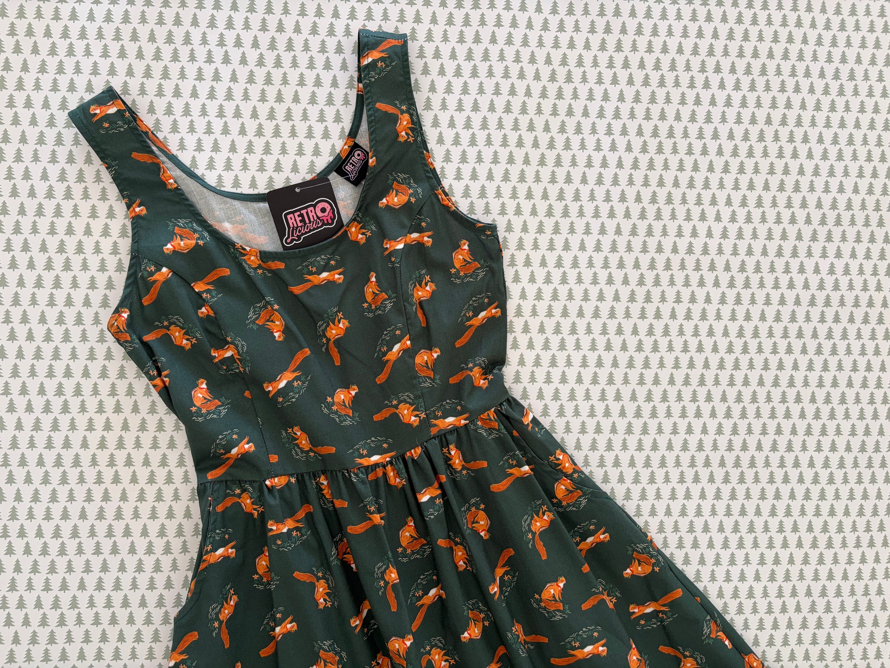 flatlay of chipmunks fit and flare dress on a pattern of trees on white background