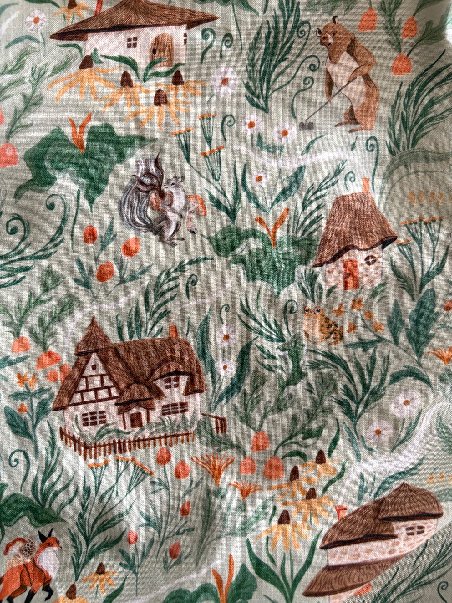Patterned fabric with houses, trees, and animals on a light background