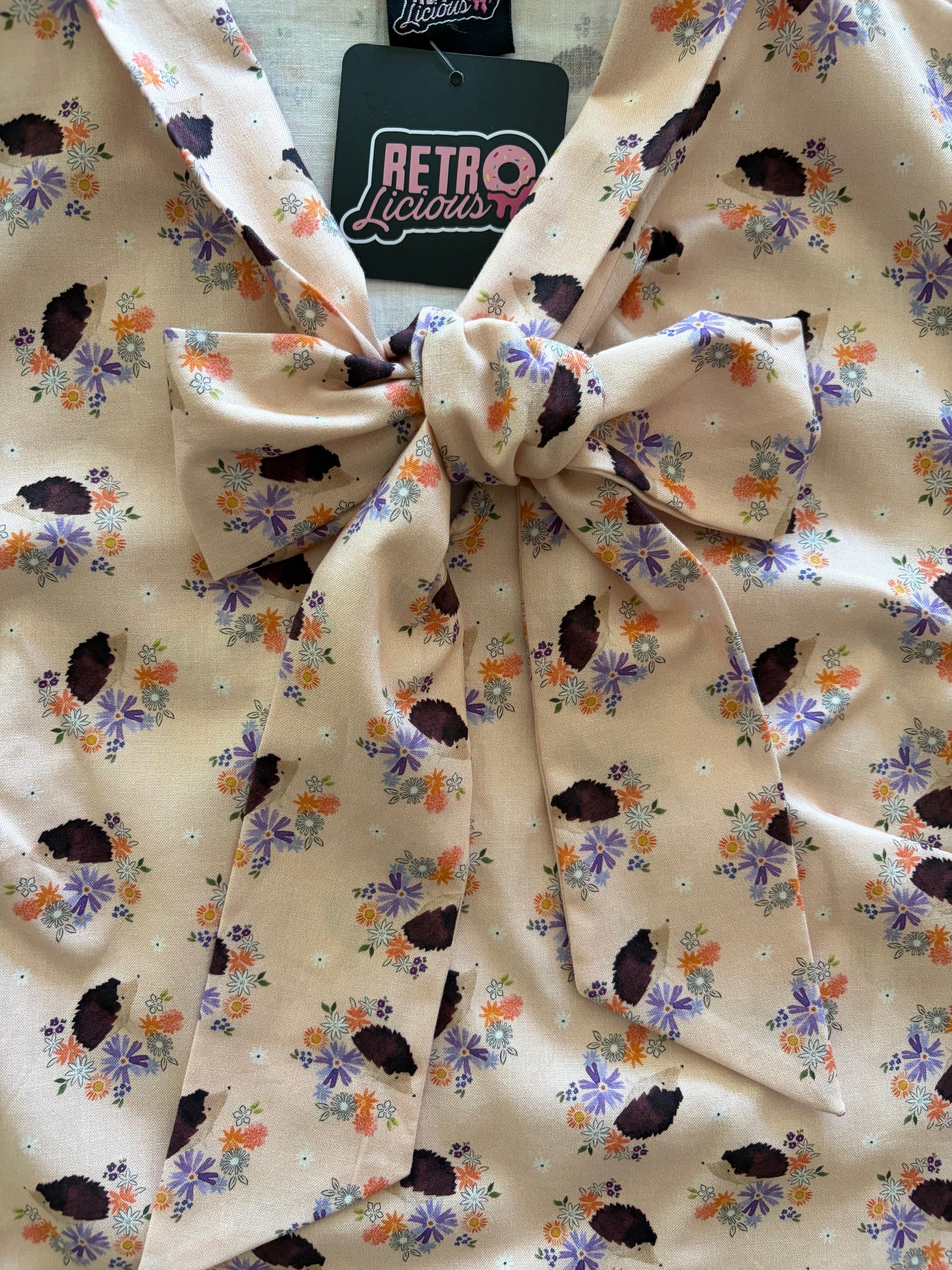 Floral patterned fabric with a bow, featuring small flowers and leaves on a beige background.