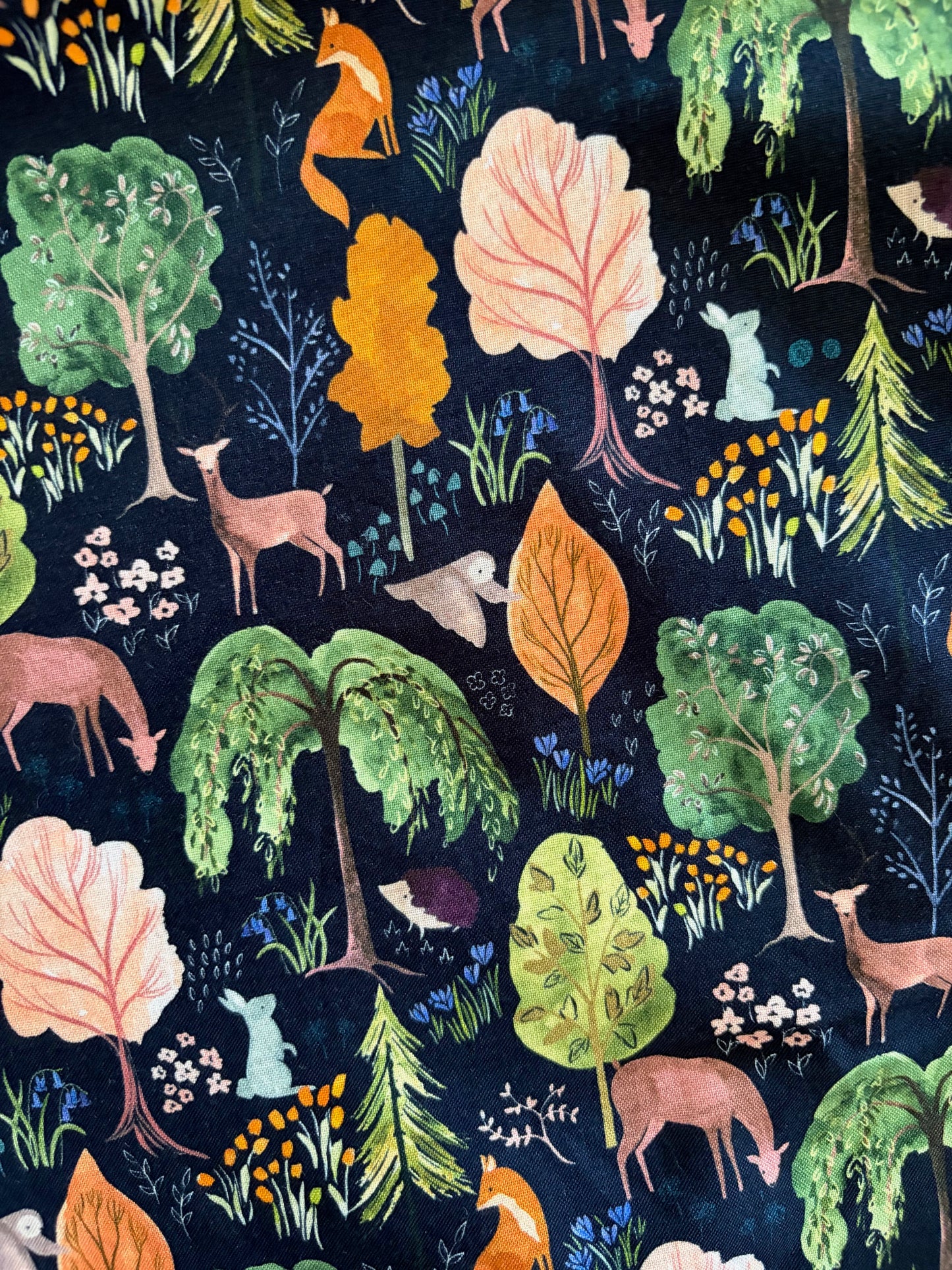 Fabric with colorful forest pattern featuring trees, animals, and leaves on a dark background