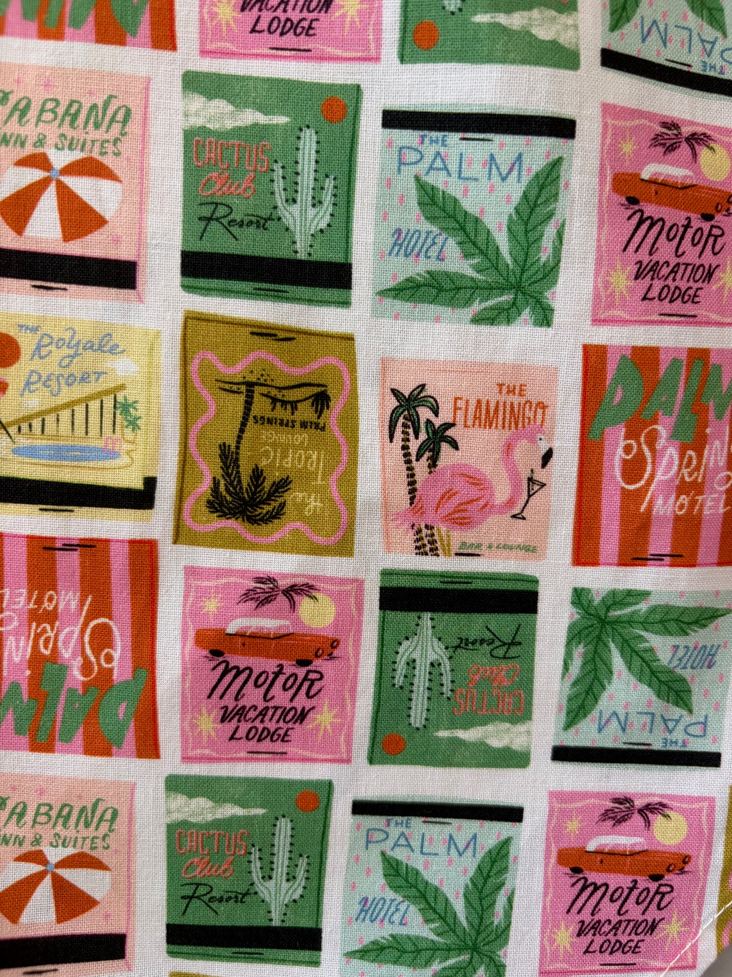 Patterned fabric with colorful designs of palm trees, leaves, and text on a white background.