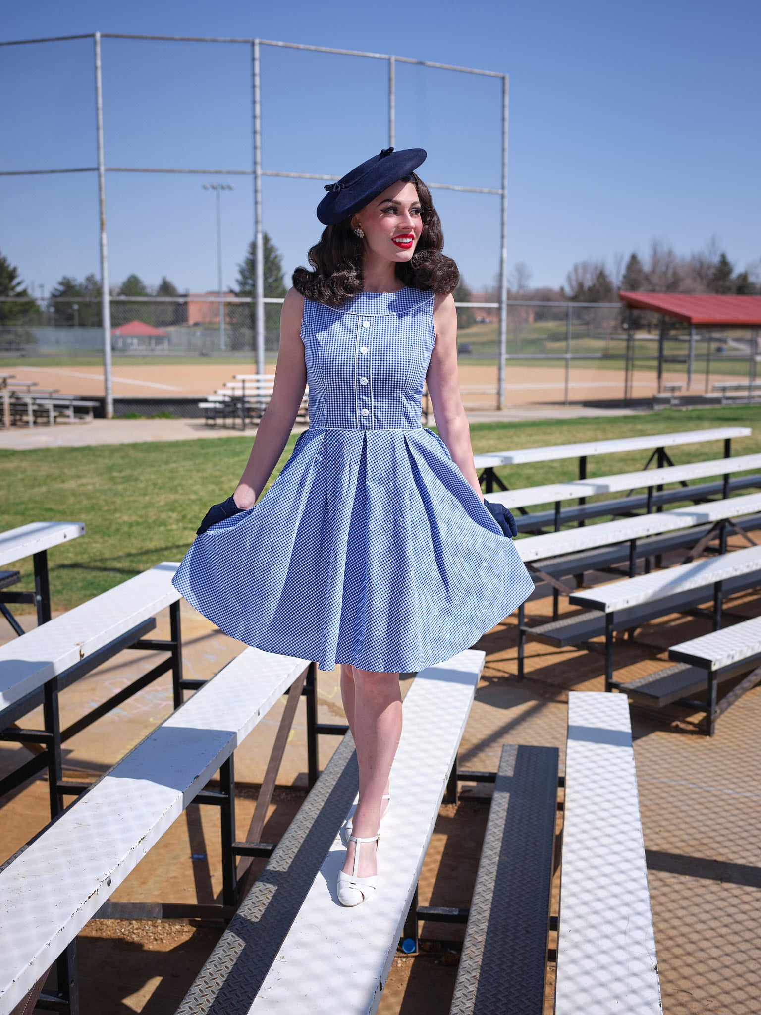 a full size of a model wearing elizabeth dress in gingham and vintage hat and gloves standibg on bleachers