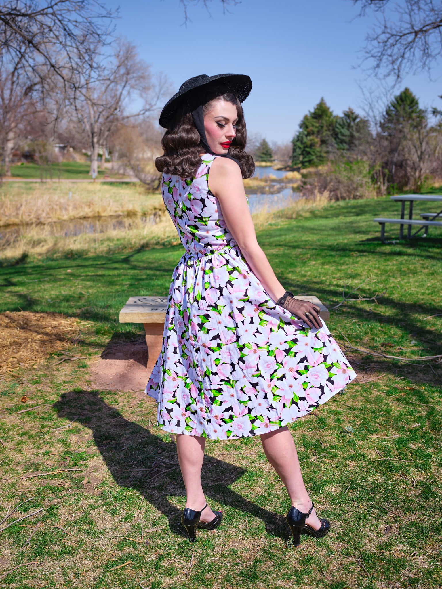 a back view of model in a park wearing magnolia midi dress and a black vintage hat
