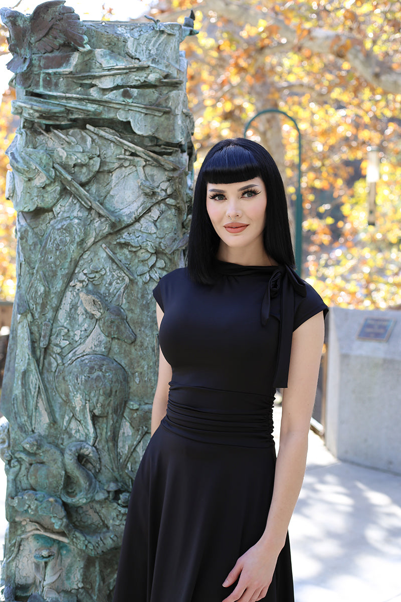 a close up of a model standing outdoors wearing the bombshell dress in black