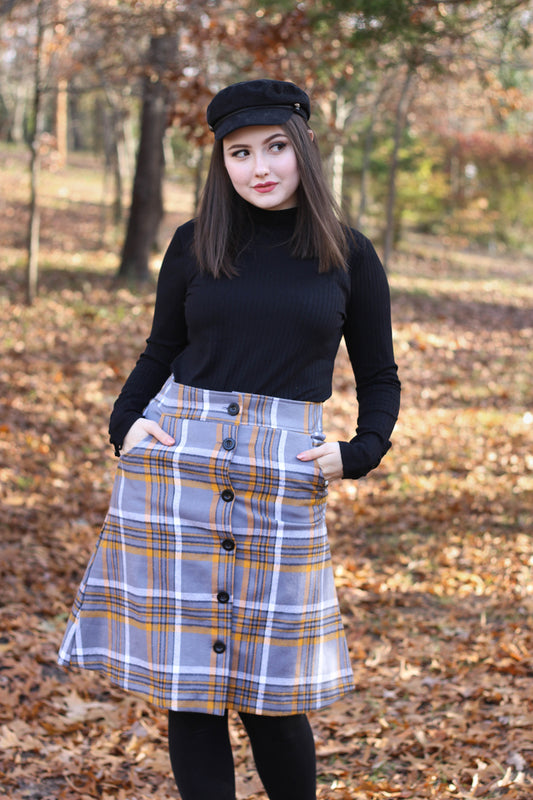 Model wearing grey plaid skirt with black beret in forest