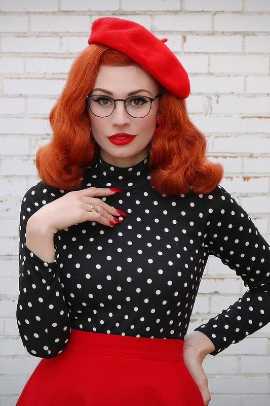 Model wearing a black top with white polka dots, red beret and red skirt.