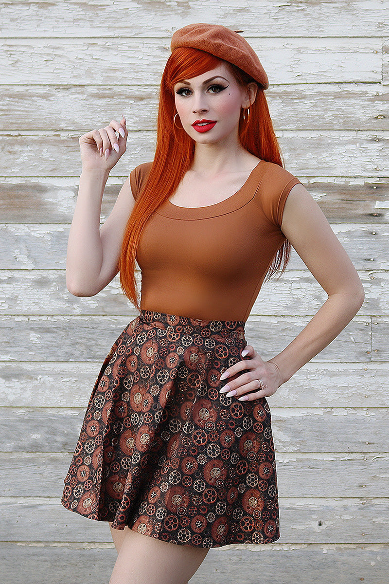 Model with red hair wearing a skater skirt and brown top.