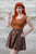 Model with red hair wearing a skater skirt and brown top.