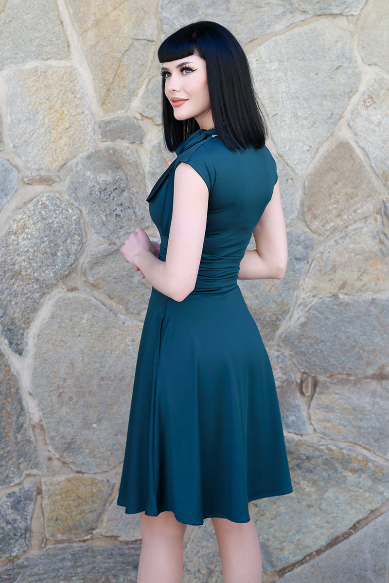 a back of a bmodel standing in front of stone wall outside wearing the bombshell dress in spruce green