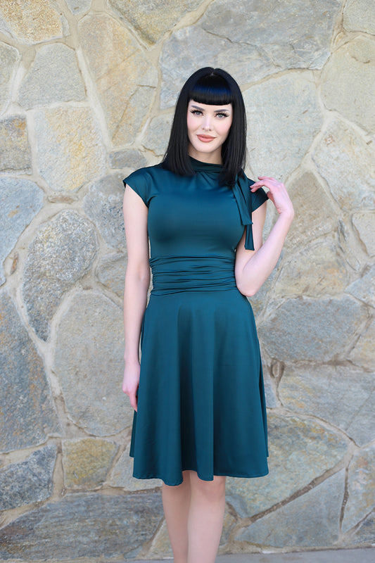 a model standing in front of stone wall outside wearing the bombshell dress in spruce green