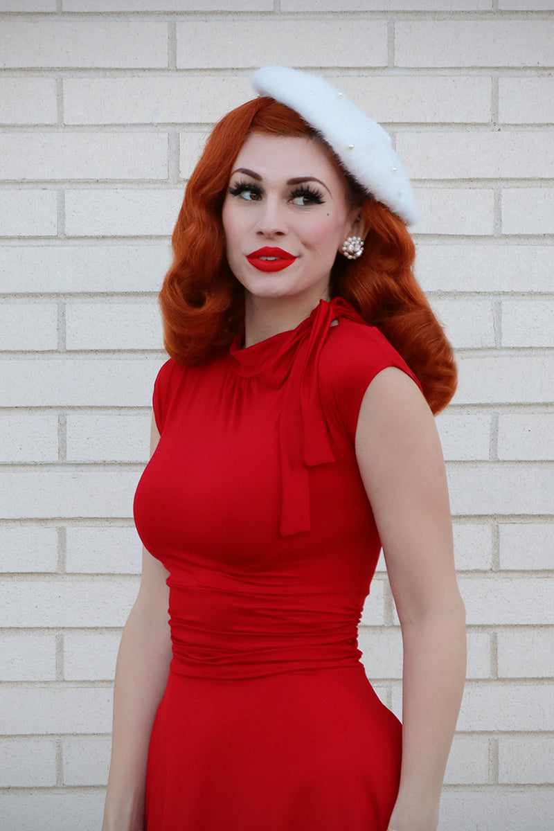 Waist level picture of model wearing a retro era sleeveless dress with a white beret.