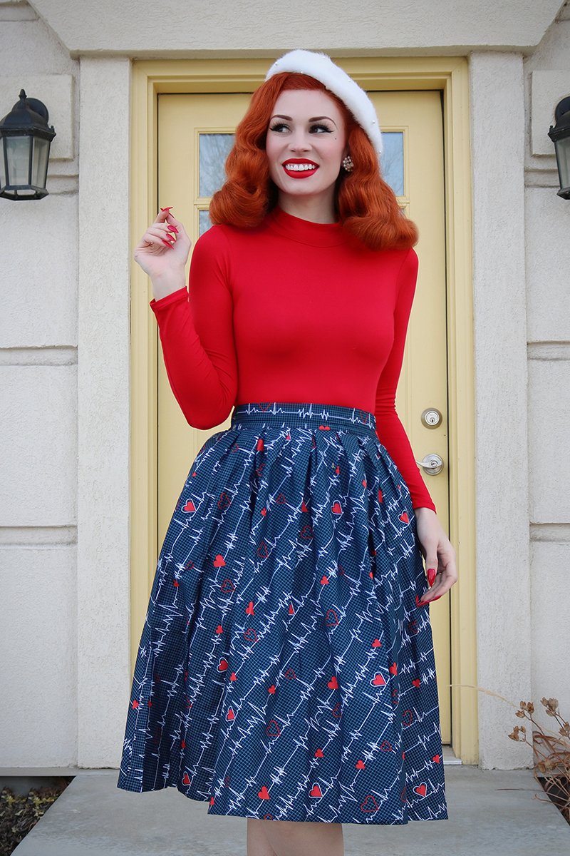 Model smiling and looking off-camera wearing a red mock turtleneck, white beret and blue retro skirt.