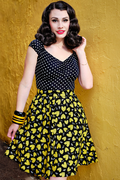 a model standing in front of a yellow wall wearing the honey hives a-line skirt with polka dots isabel top
