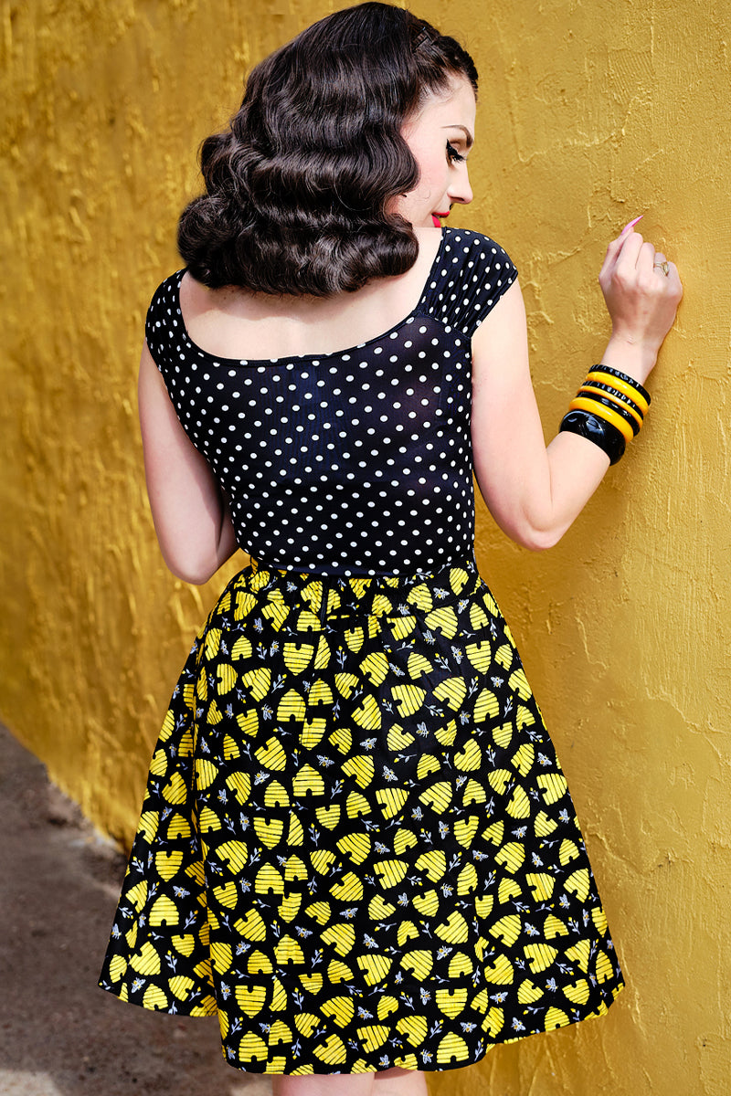 a back view of model standing in front of a yellow wall wearing the honey hives a-line skirt with polka dots isabel top