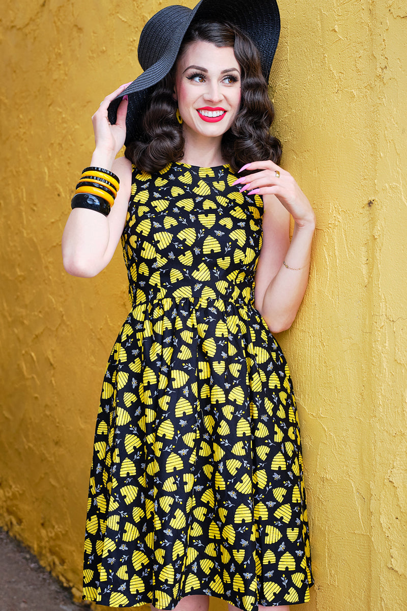 a model wearing a honey hives vintage dress and black hat leaning against a yellow wall